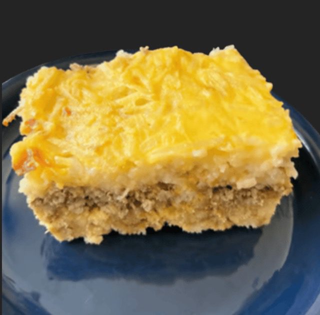 A portion of Homemade Sausage Egg Bake on a blue plate, showcasing its cheese topping and visible layer of ground meat.